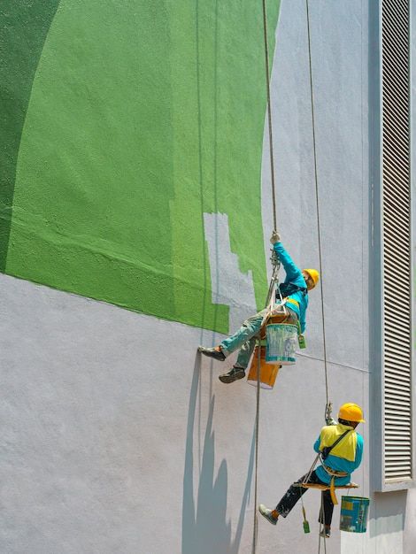 dois homens pintando a fachada de um prédio de verde