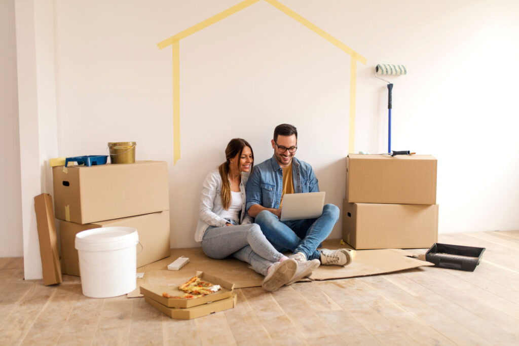 um casal sentado no chão sorrindo no meio de uma pintura residencial