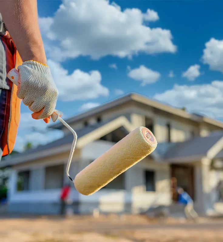um homem com um pincel na mão em frente a uma casa